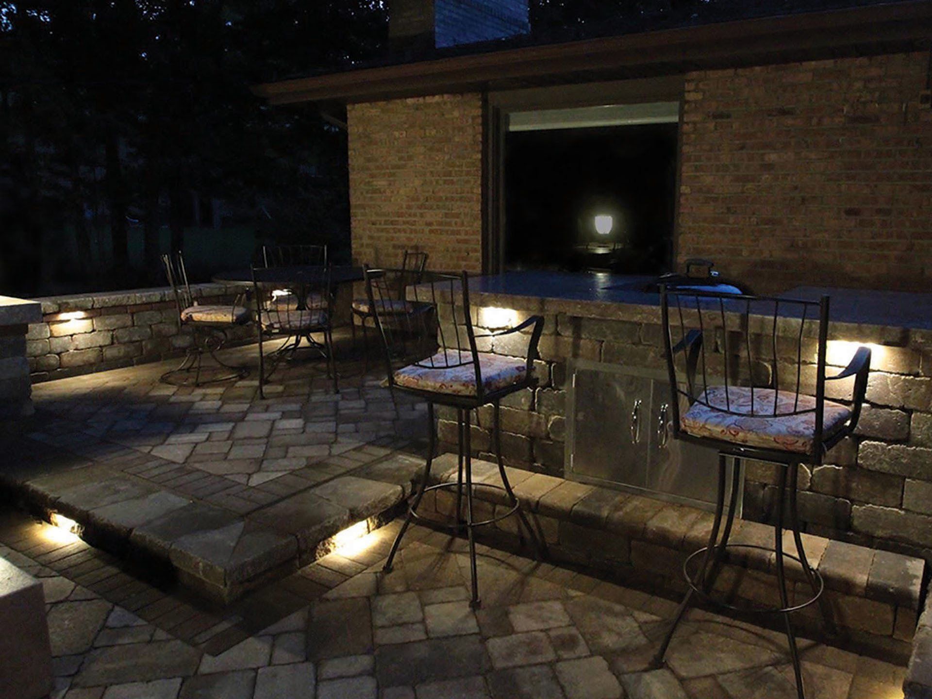 a brick patio with a bar and chairs at night