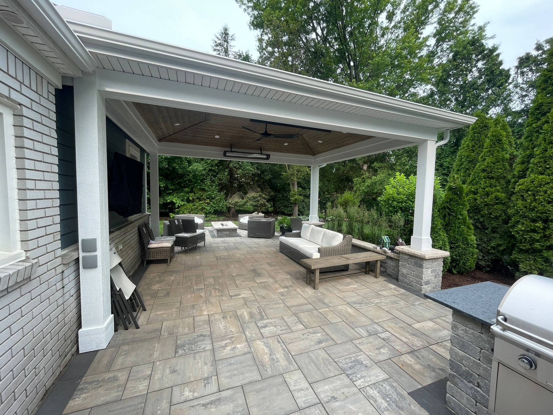 A large covered patio with a couch, chairs, and a grill.