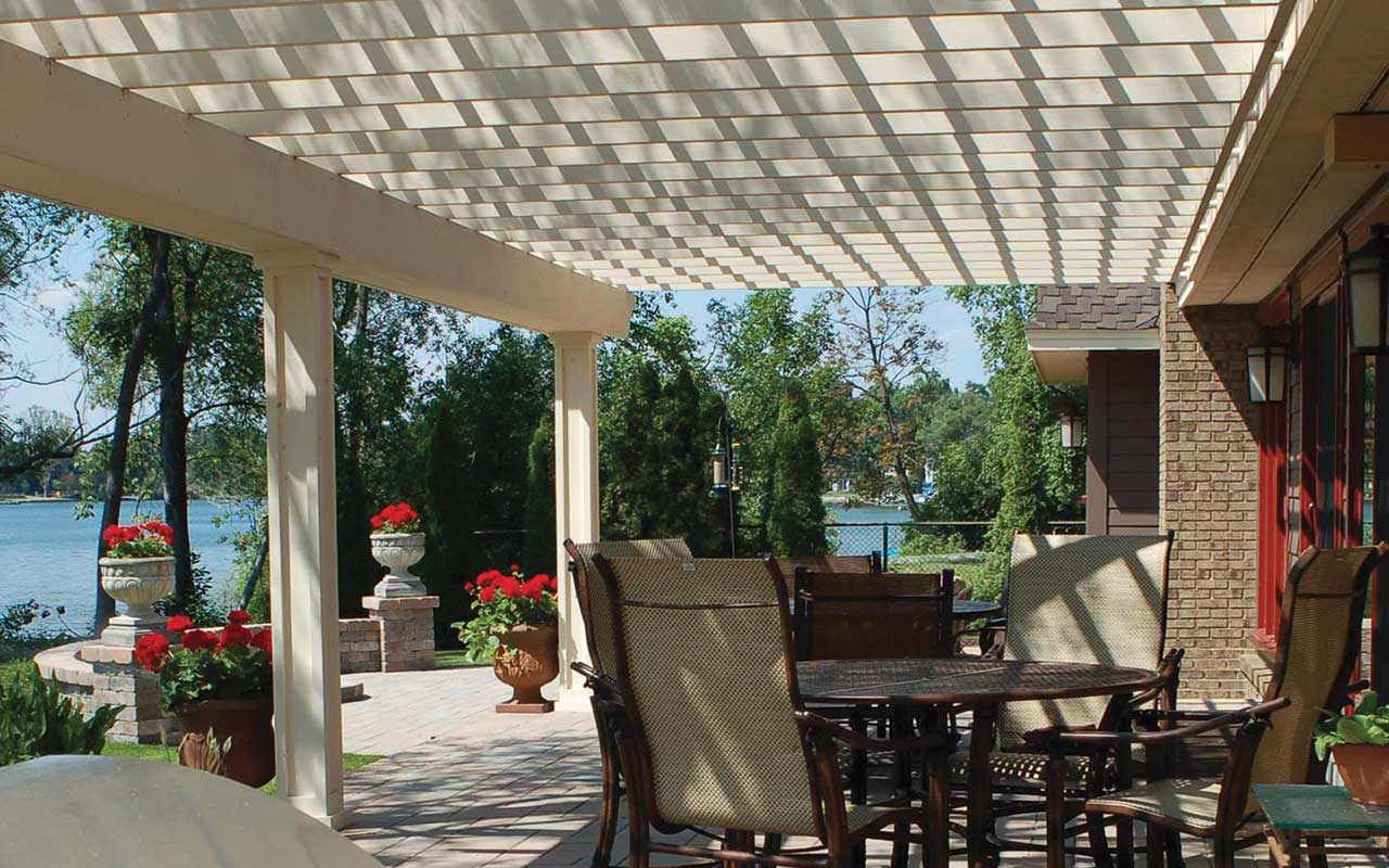 a patio with a table and chairs under a pergola overlooking a lake .