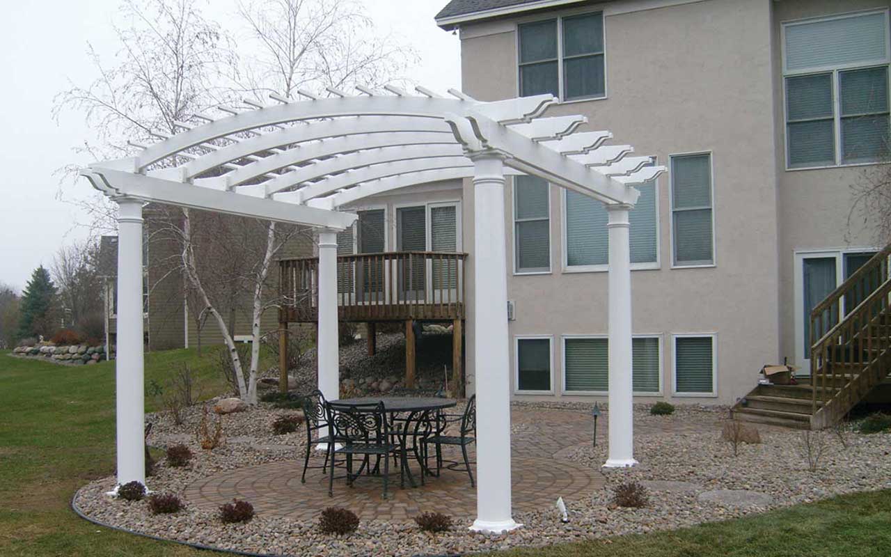 a white pergola with a table and chairs underneath it in front of a house .