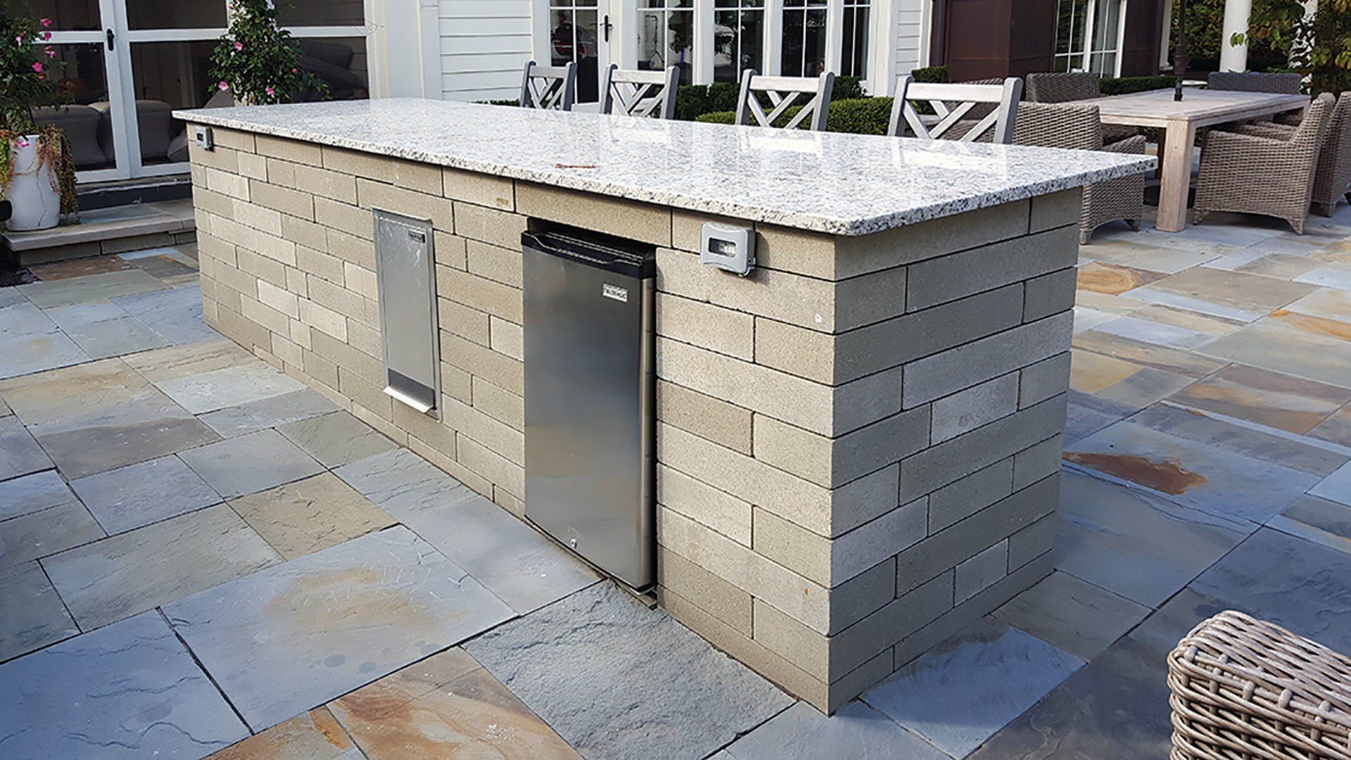 a brick island with a granite counter top and a stainless steel refrigerator .