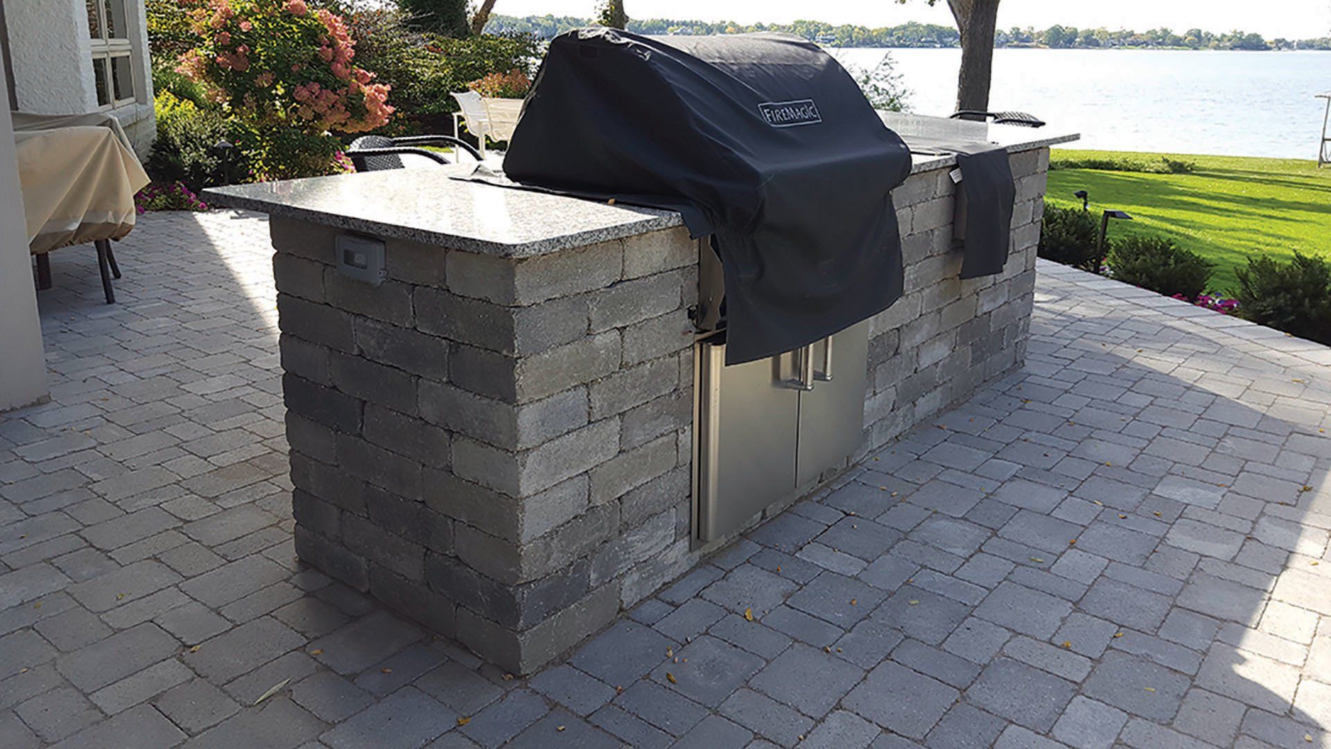 a grill with a black cover is sitting on a brick patio