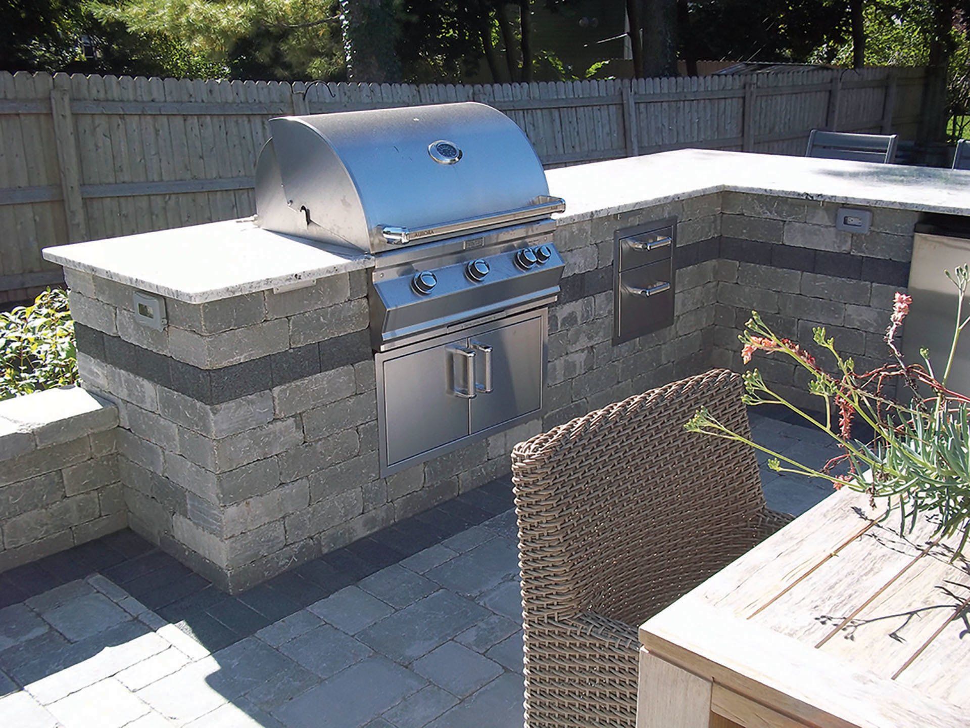 an outdoor kitchen with a grill and a wicker chair