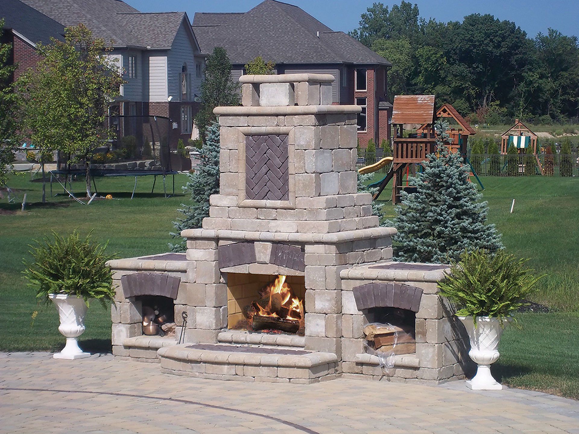 a brick fireplace is surrounded by potted plants and a playground in the background