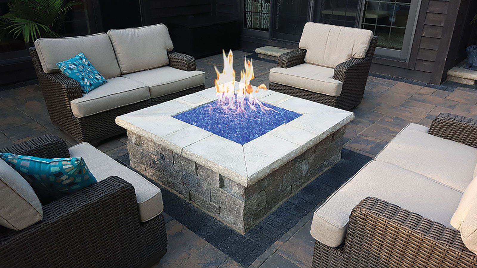 a fire pit is surrounded by wicker furniture on a patio .