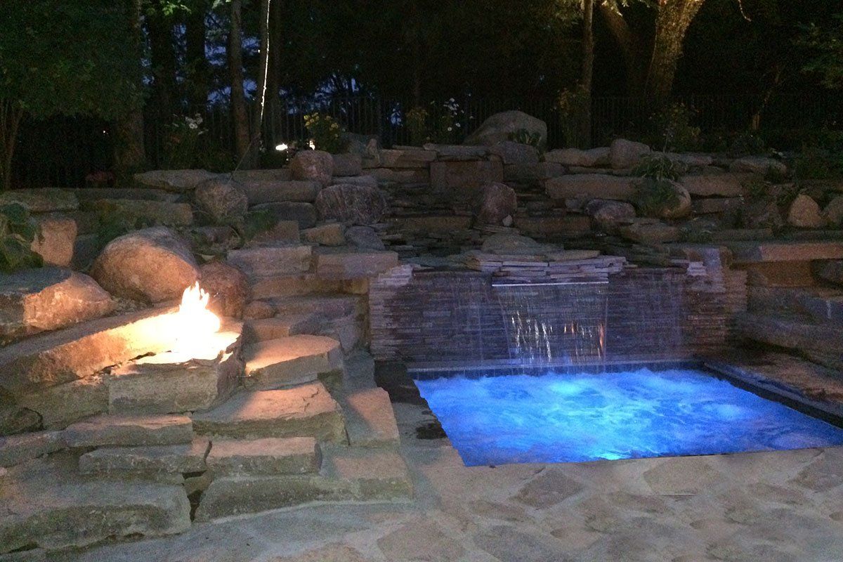 a swimming pool with a fire pit and a waterfall at night .
