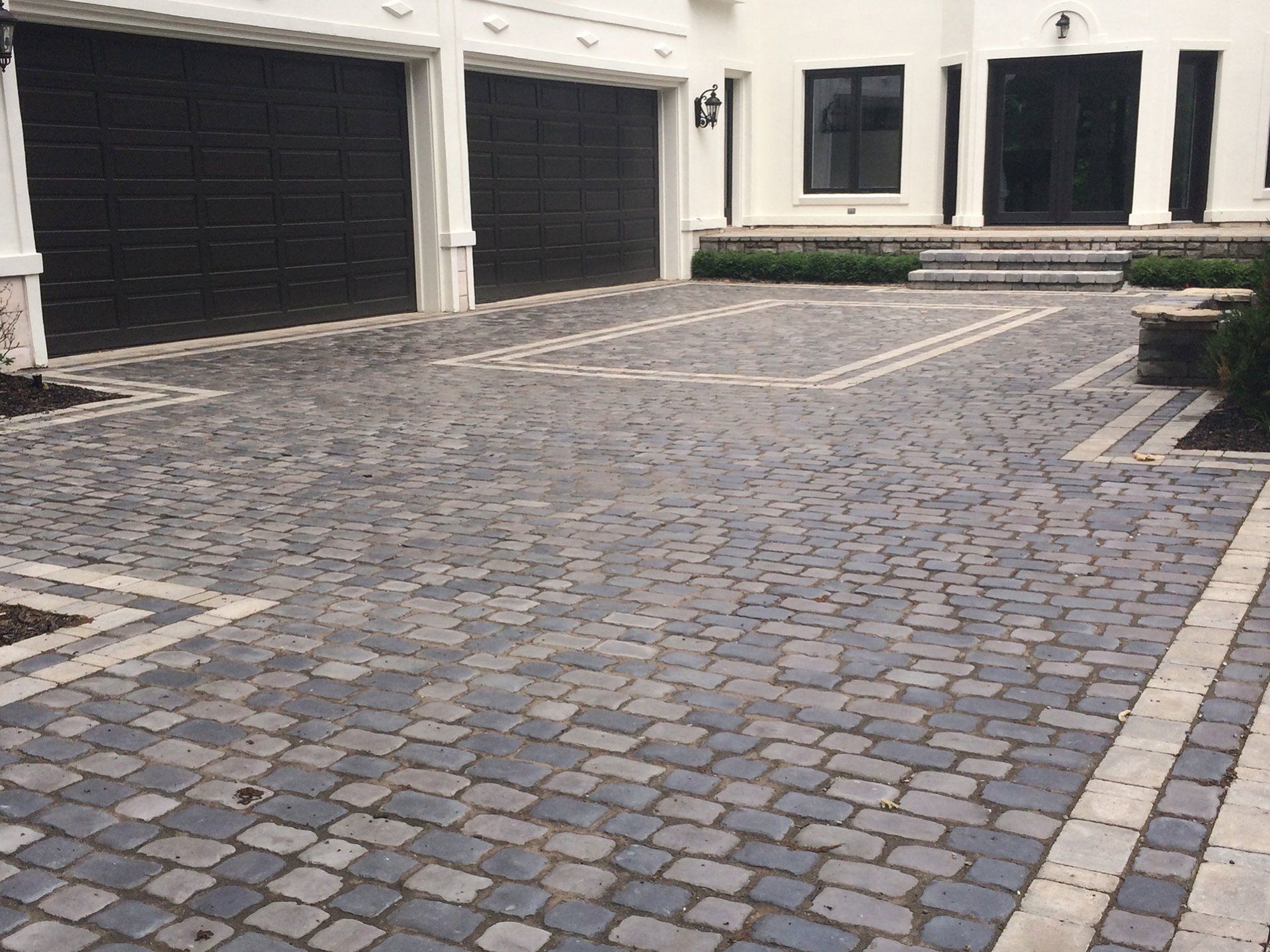 a cobblestone driveway in front of a house with two garage doors .