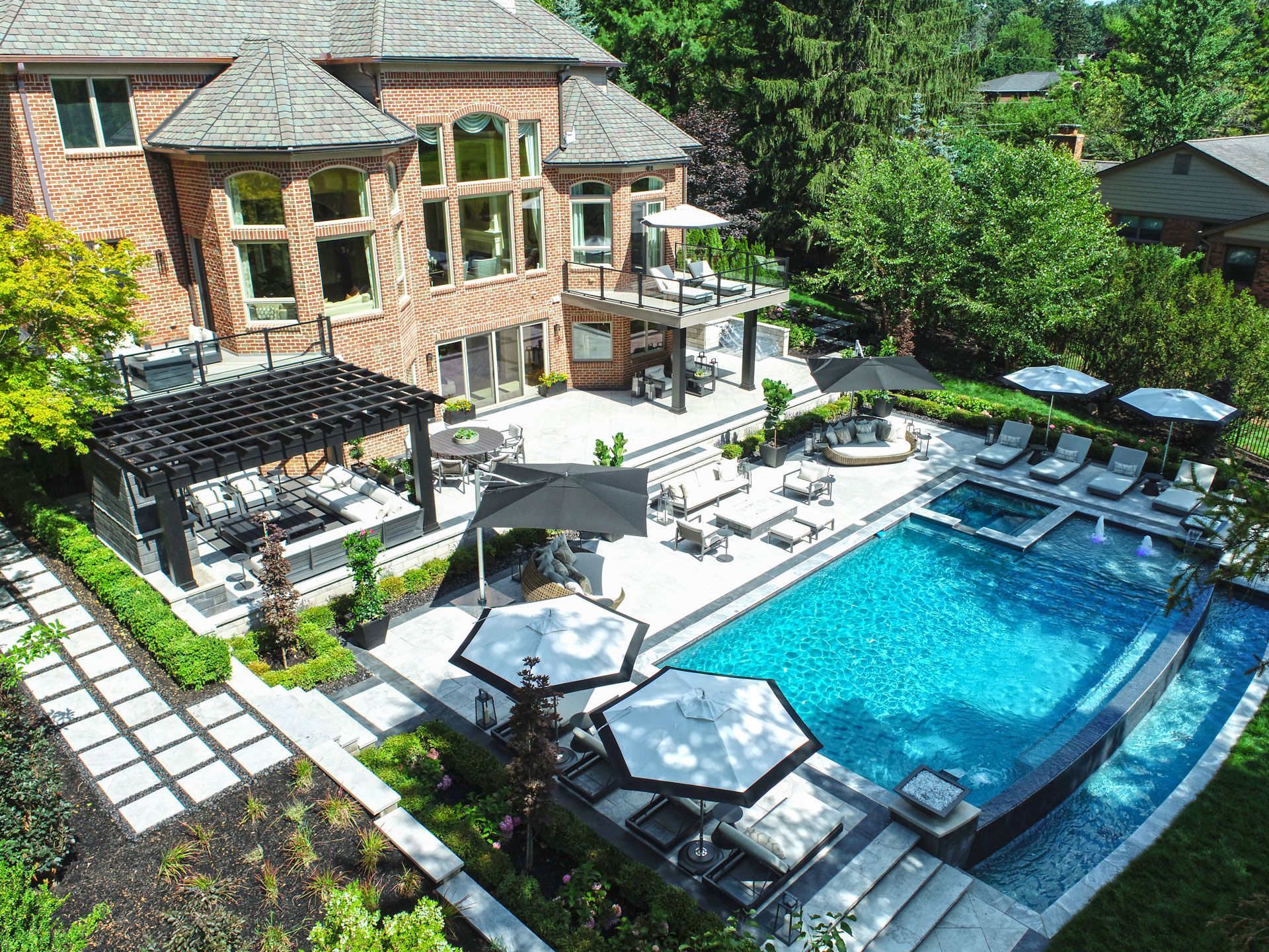 an aerial view of a large swimming pool surrounded by chairs and umbrellas in front of a large brick house .