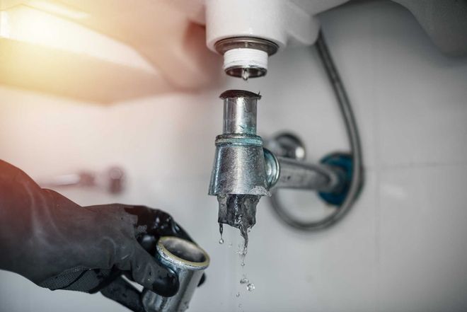Gloved hand shutting off a dripping faucet over a sink with water splashing below