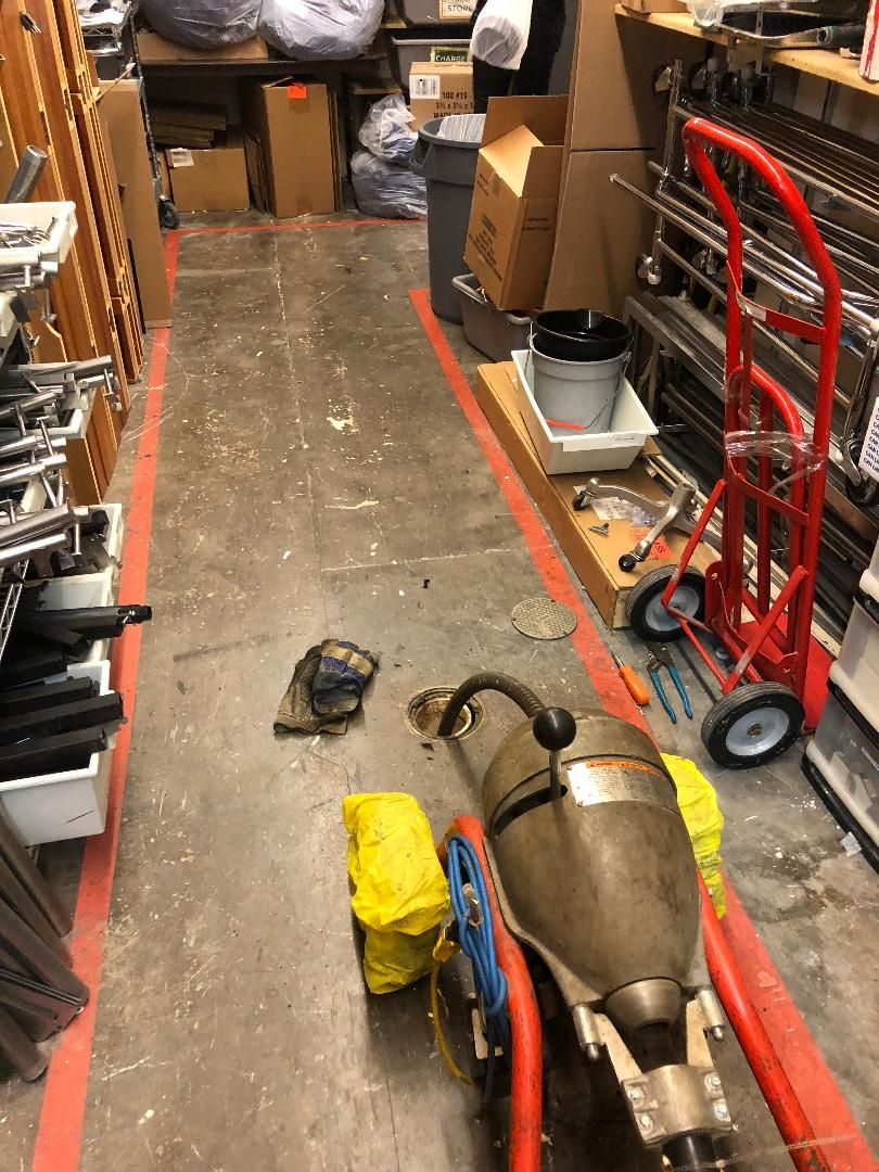 Narrow cluttered storage aisle with tools and boxes, a red hand truck, and equipment on the floor