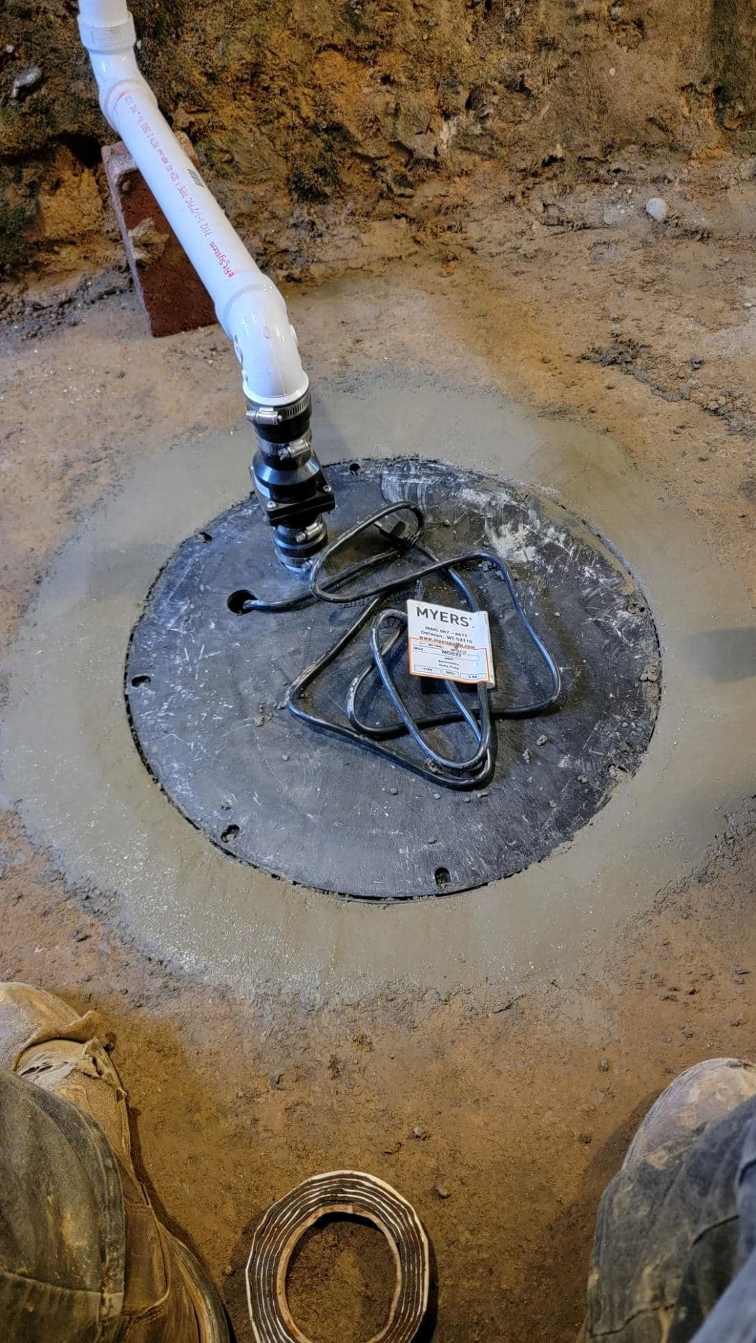 White pipe connected to a round black underground access cover in a dirt trench