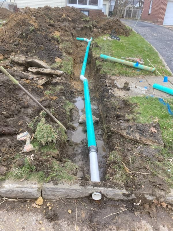 Blue pipe trench across muddy yard beside a pile of excavated soil and a driveway