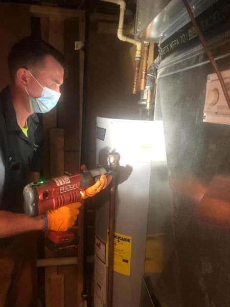 Technician in a mask uses a red tool to inspect an electrical panel in a utility room