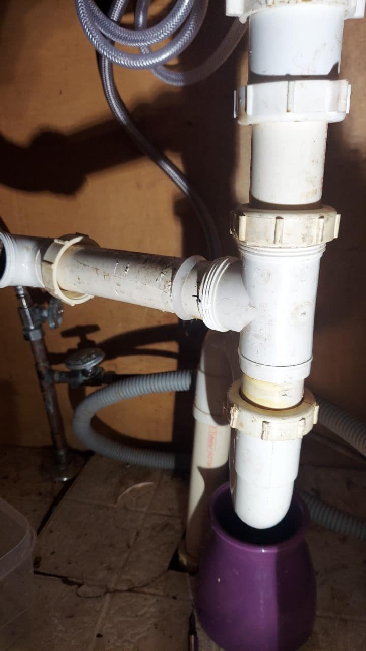 Under-sink plumbing with white PVC pipes and a purple drain bucket catching water