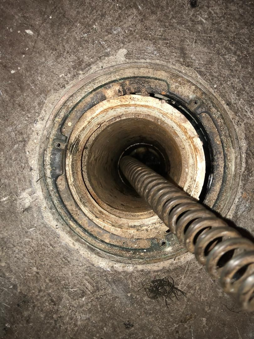 Coiled drain snake inside a circular pipe opening, viewed from above