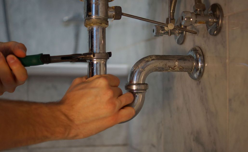 Hands using a wrench to tighten a pipe under a sink during plumbing work