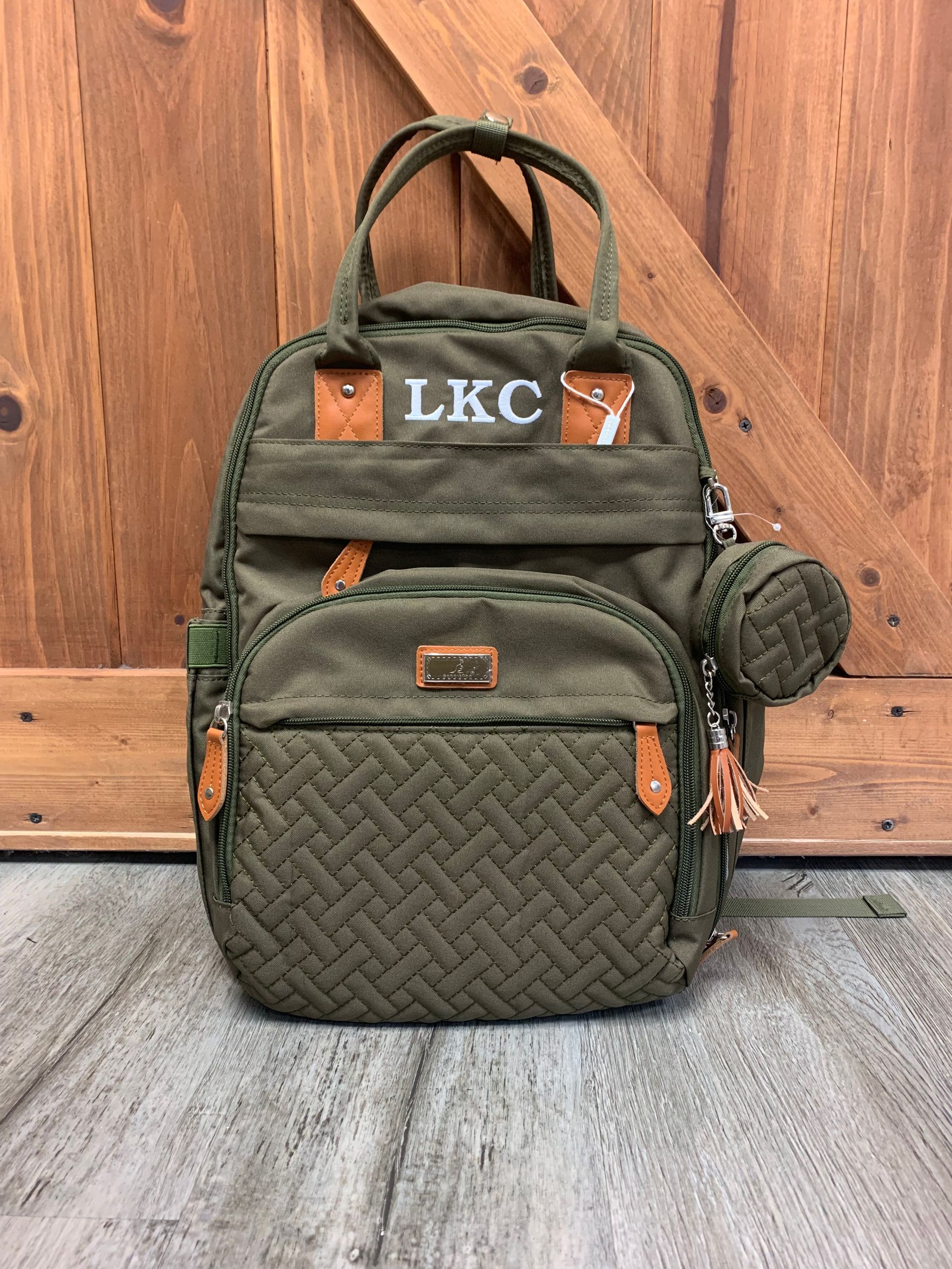 A green backpack with the letters lkc on it is sitting in front of a wooden door.