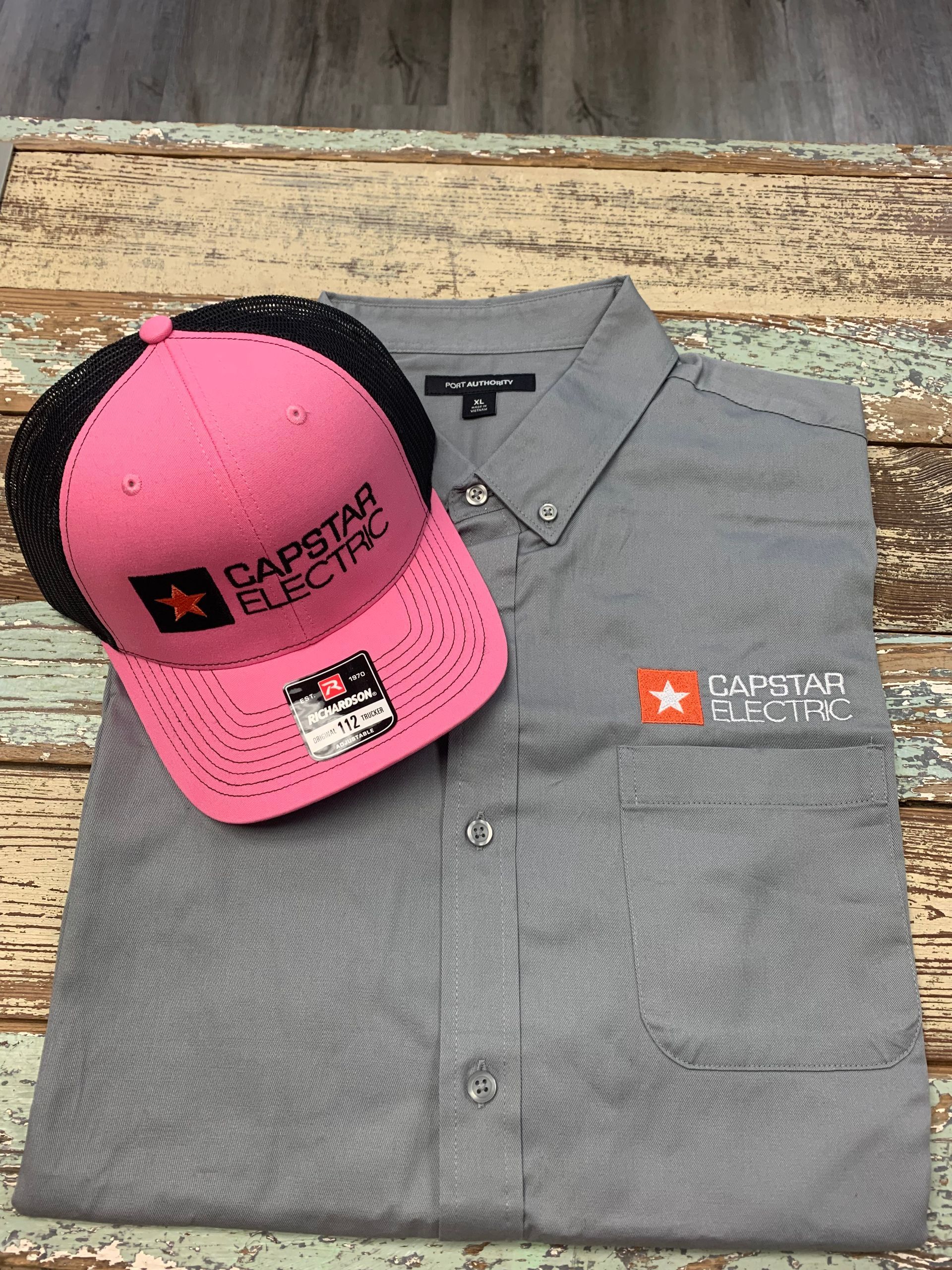 A gray shirt and a pink hat are on a wooden table.