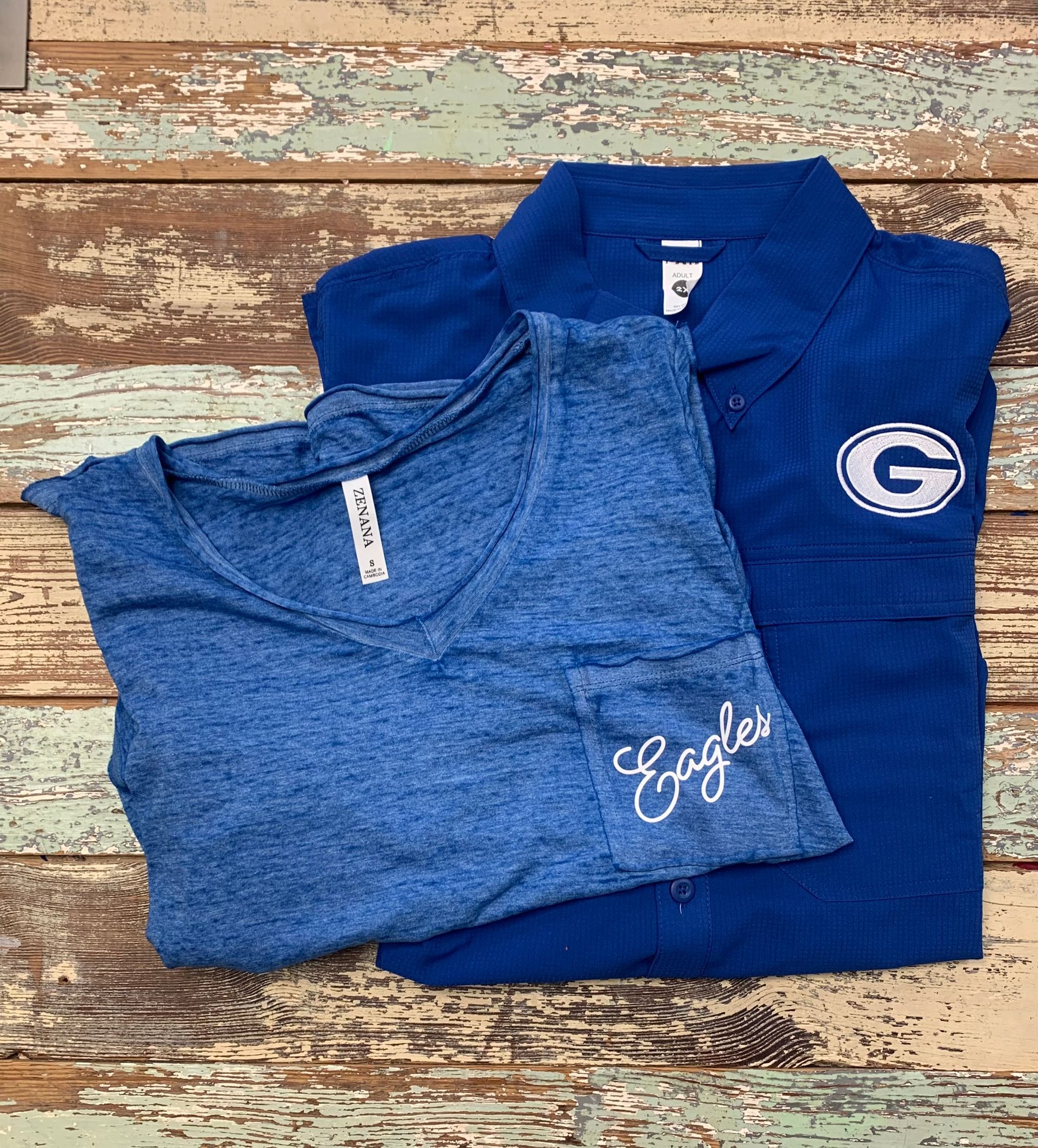 Two blue shirts are stacked on top of each other on a wooden table.