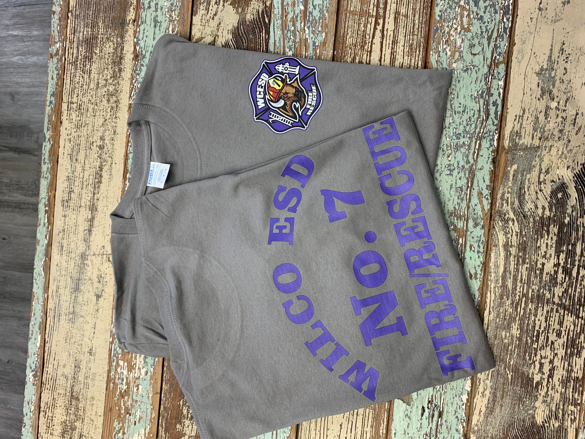 A grey shirt with purple writing on it is on a wooden table.
