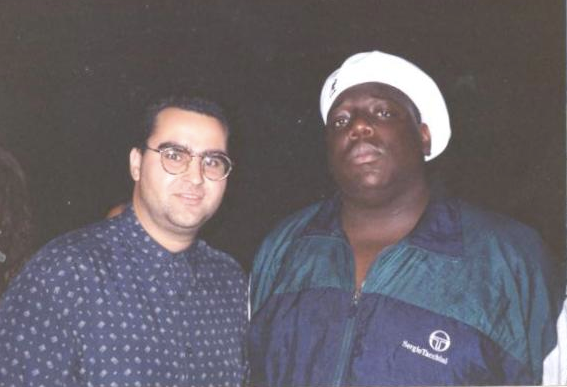 Man with glasses poses next to the rapper The Notorious B.I.G., both facing the camera.