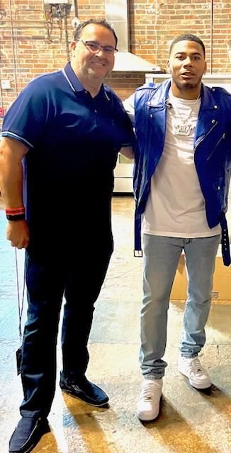 Man in blue shirt and another in blue jacket pose together indoors.