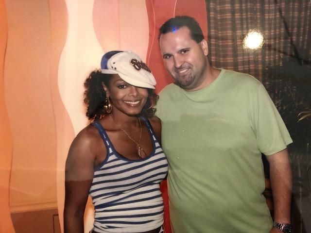 Woman in striped tank top and hat poses with a smiling man in a green shirt.