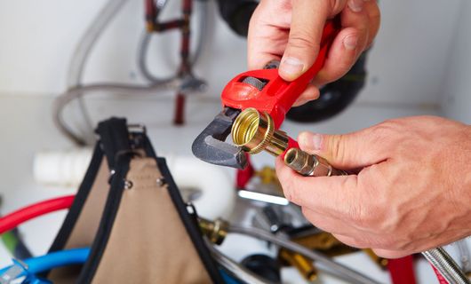 Learn More About Commercial Plumbing Plumber uses a wrench on a brass fitting in a utility area with plumbing pipes.