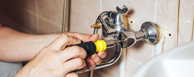 faucet repair Person using a screwdriver to repair a chrome faucet on a tiled wall.