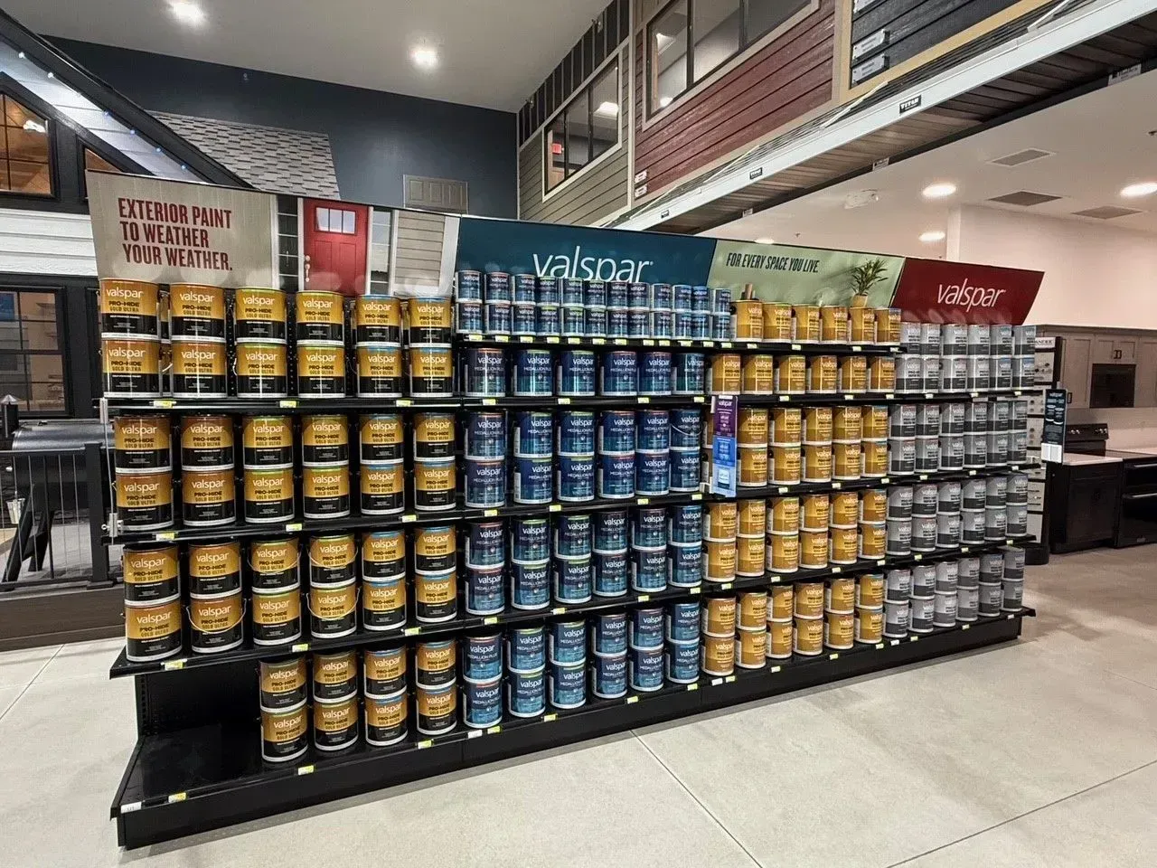 Paint cans on display in a store, organized by color and brand, with signs above.