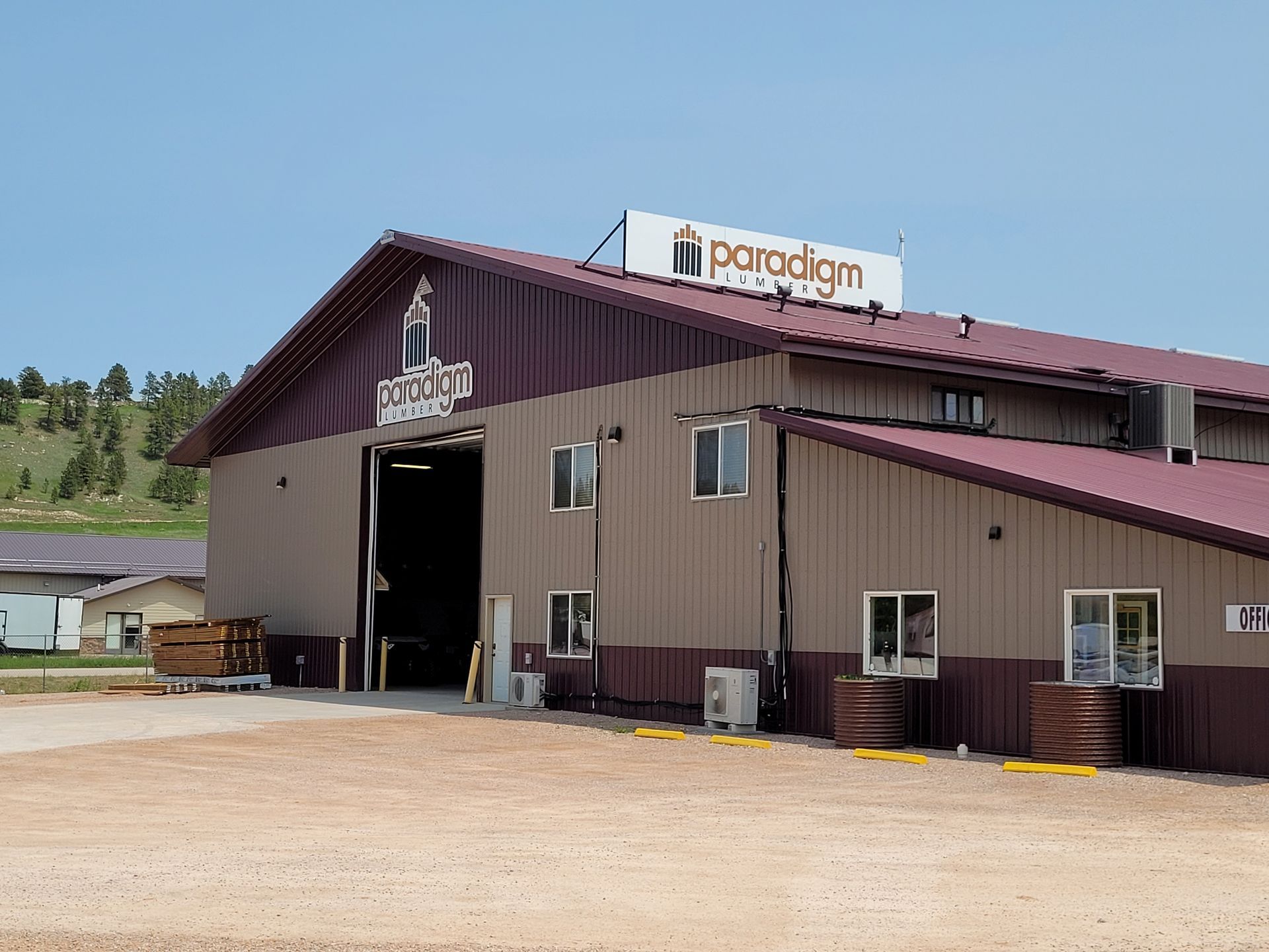 Brown and tan industrial building with Paradigm sign, large open door, and gravel lot.