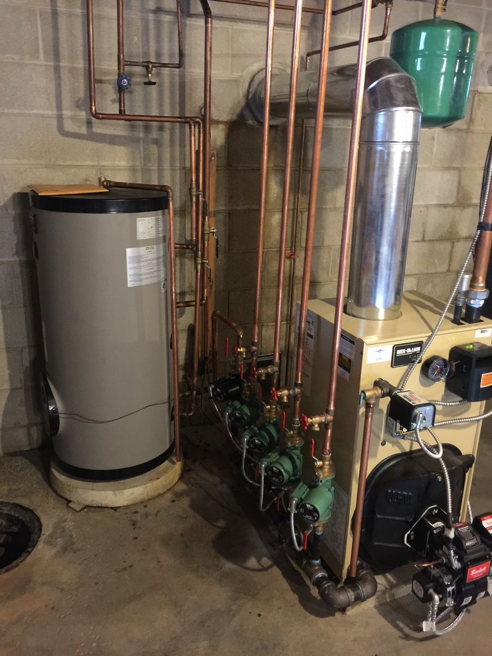 Utility room HVAC/water heater equipment: gray tanks, pipes, and a blower on a concrete pad.