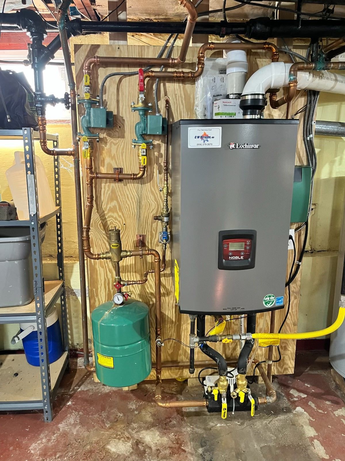 Basement utility area with a gray water heater, pipes, valves, and a green pump tank on the floor