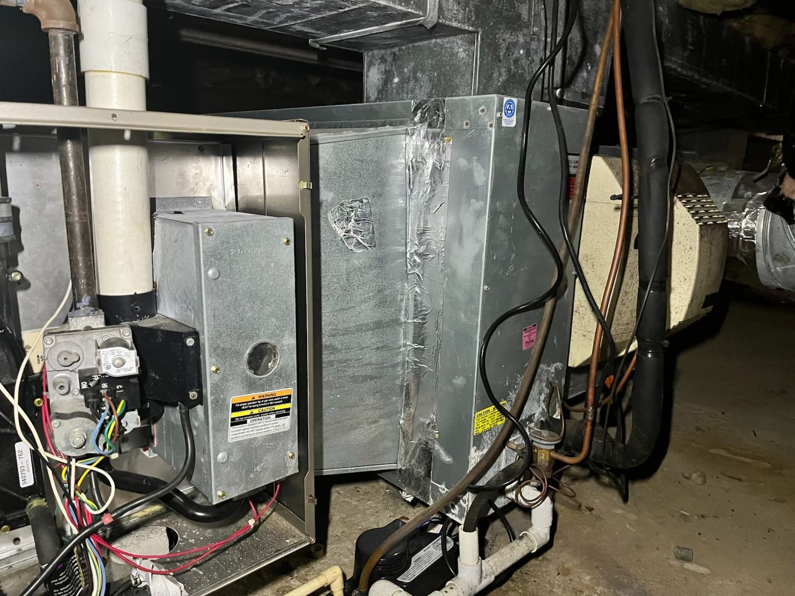 Basement wall with electrical panel, white pipes, and utility equipment under exposed ceiling beams