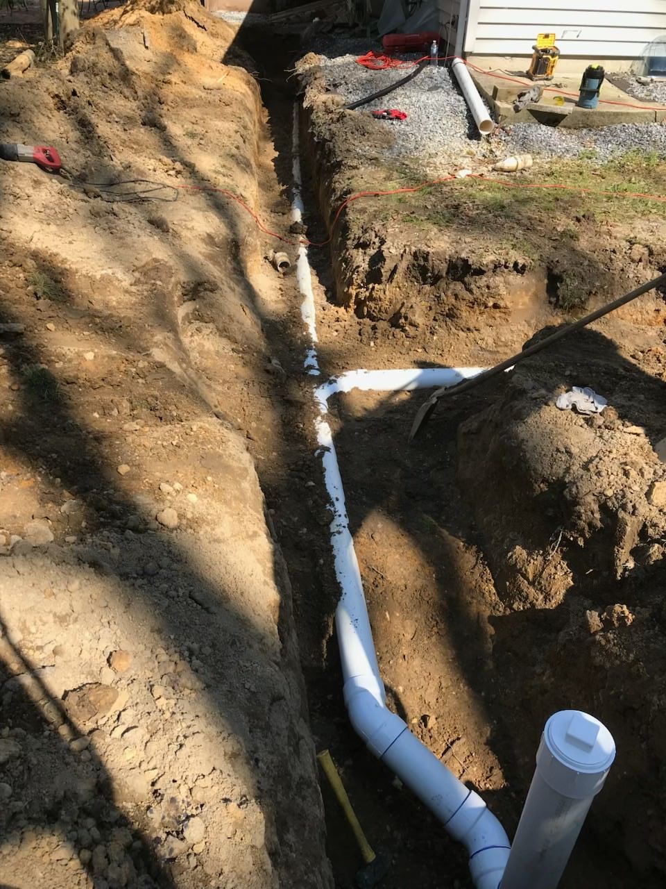 Trenched yard with white PVC pipes and an open drainage line in dirt under construction