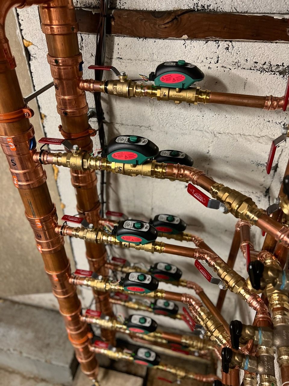 Copper plumbing pipes with several green shutoff valves in a utility room