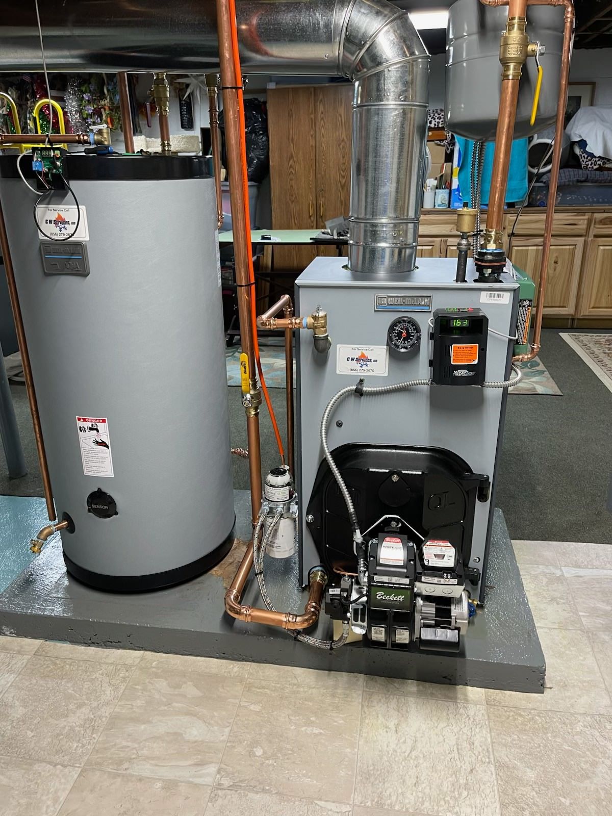 Water heater and boiler equipment in a utility room with exposed pipes and ducting.
