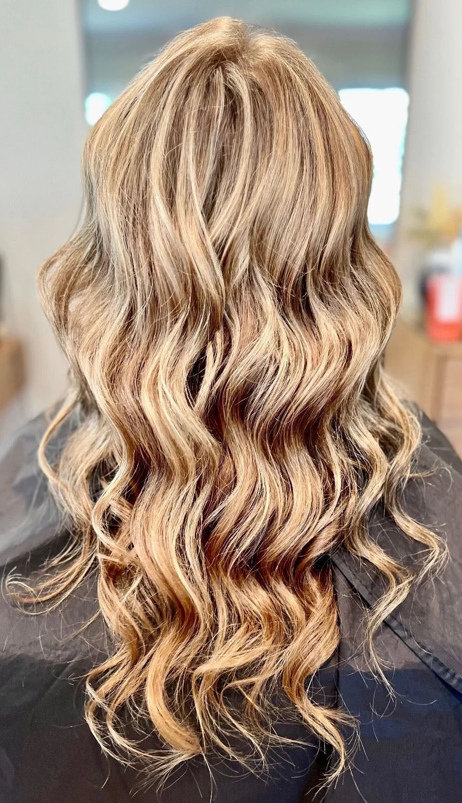 The back view of hair styled in long, wavy, golden-brown highlights against a neutral background.