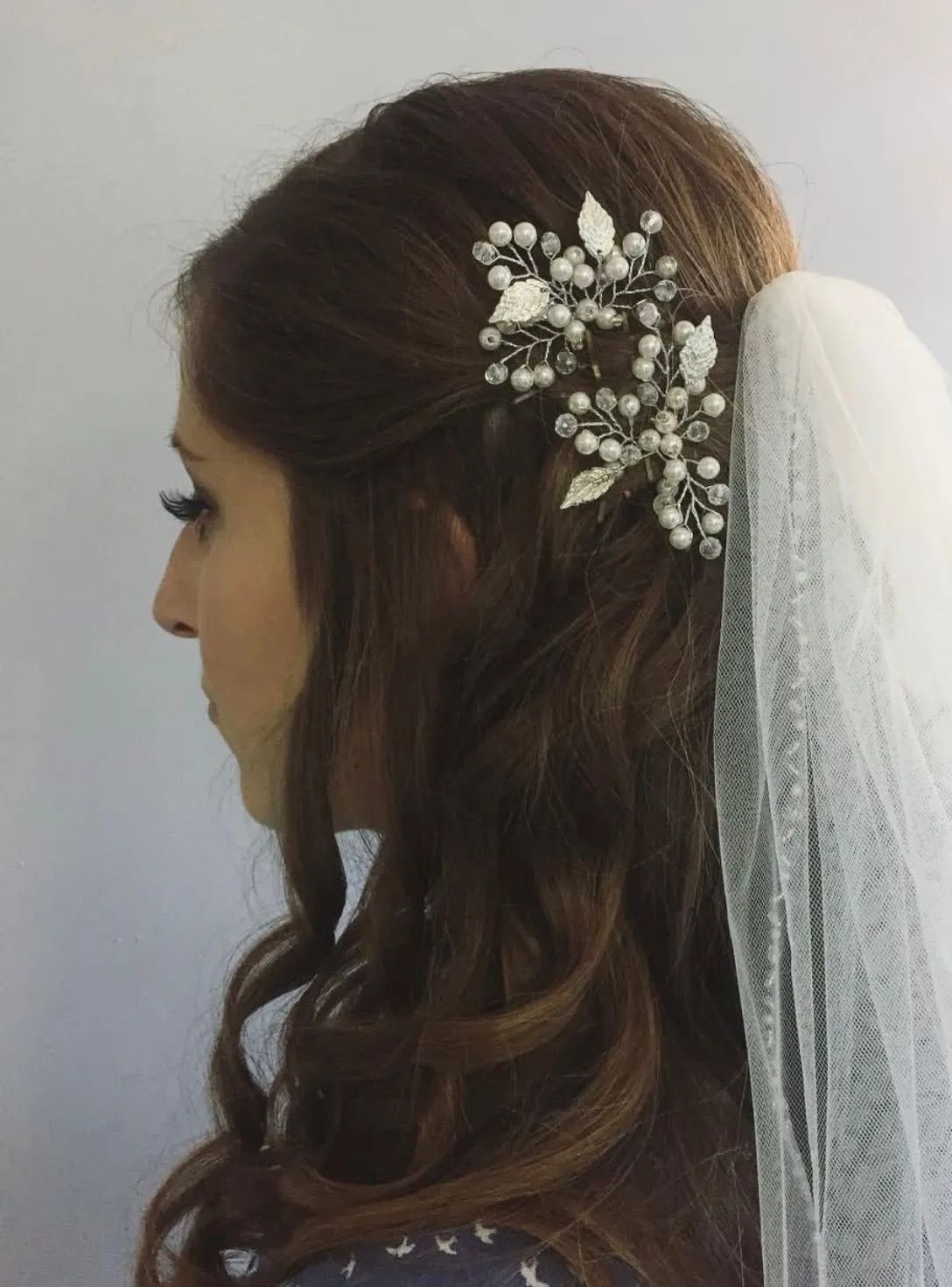 Side profile of a person wearing a delicate silver floral headpiece with pearls and a wedding veil in their brown hair.