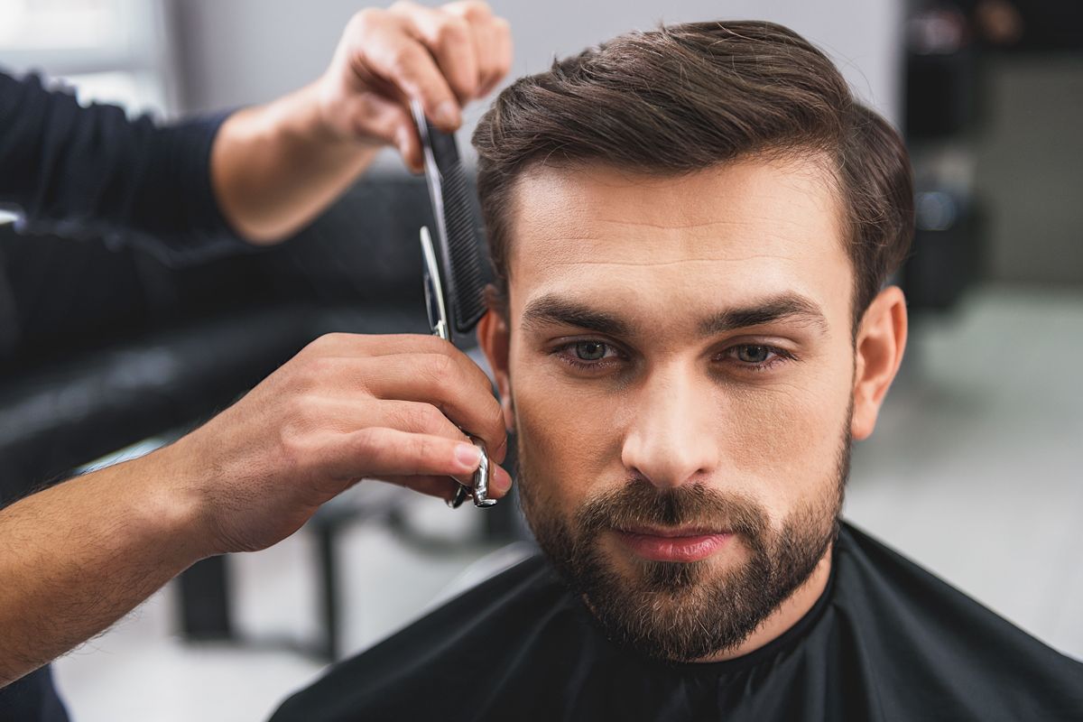 A stylist uses scissors and a comb to trim the hair of a person seated in a salon chair.