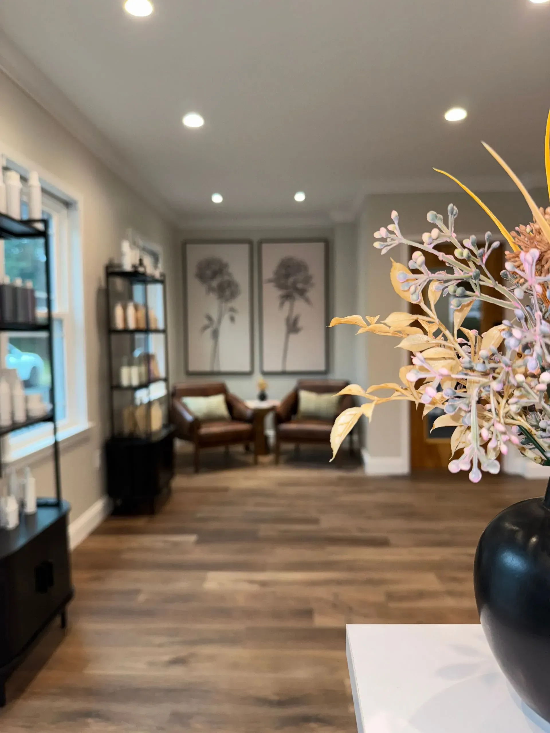 A waiting area with two brown leather armchairs, botanical framed prints, and a decorative flower arrangement in front.