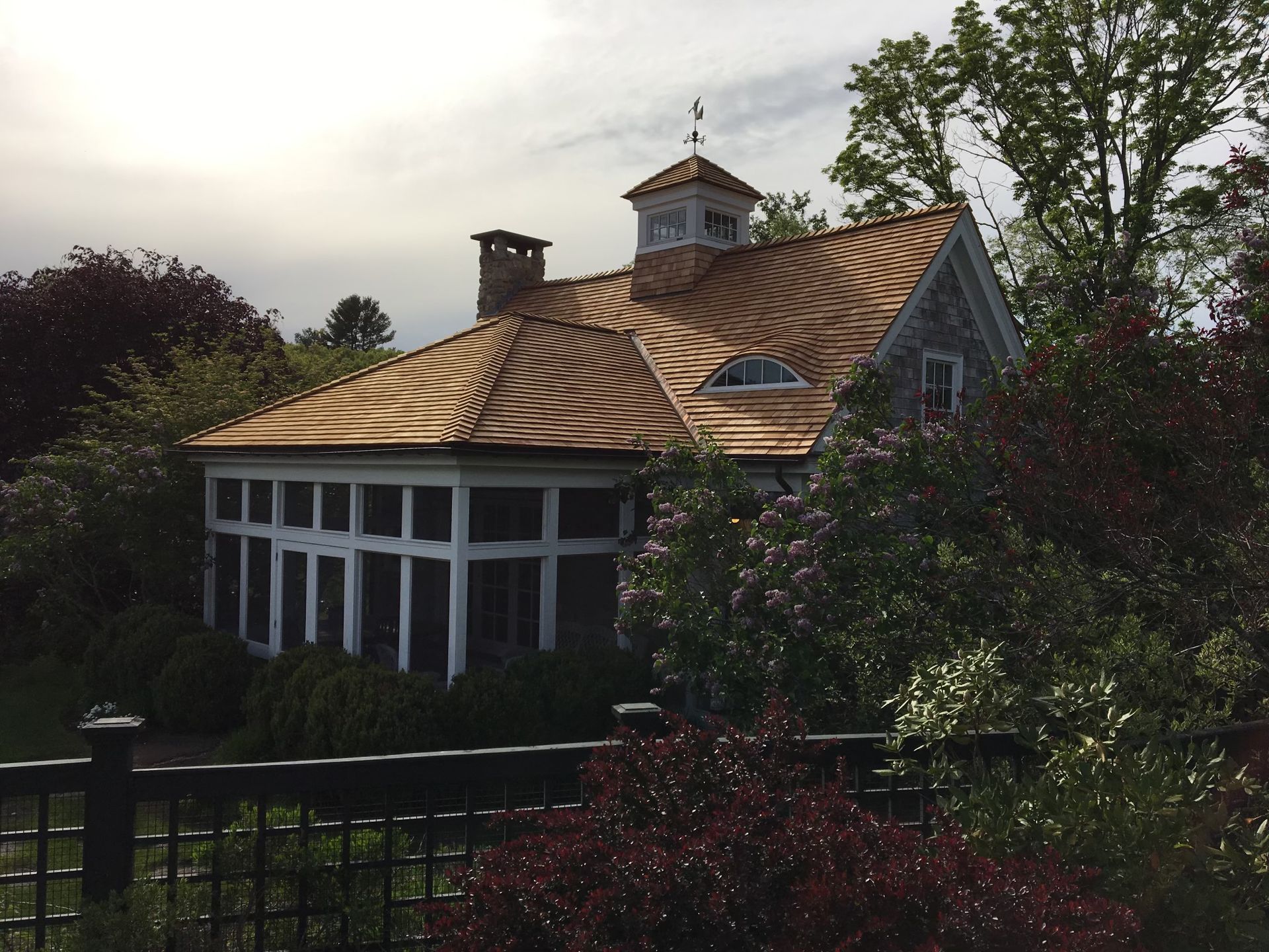 A house with a shingle roof is surrounded by trees and bushes