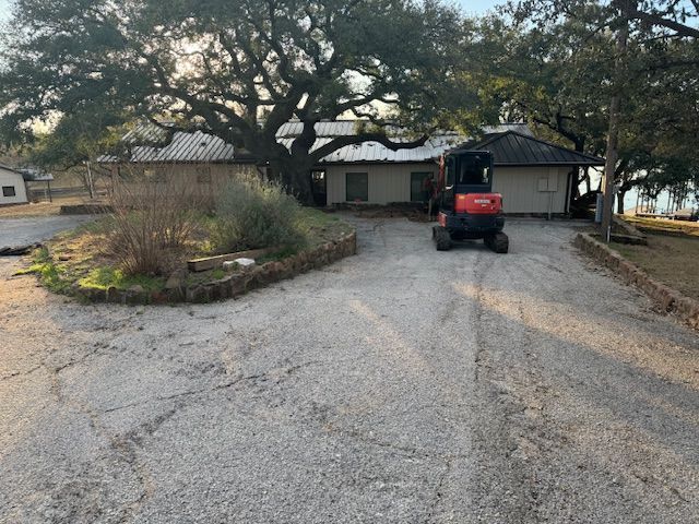 A tractor is driving down a gravel road in front of a house.