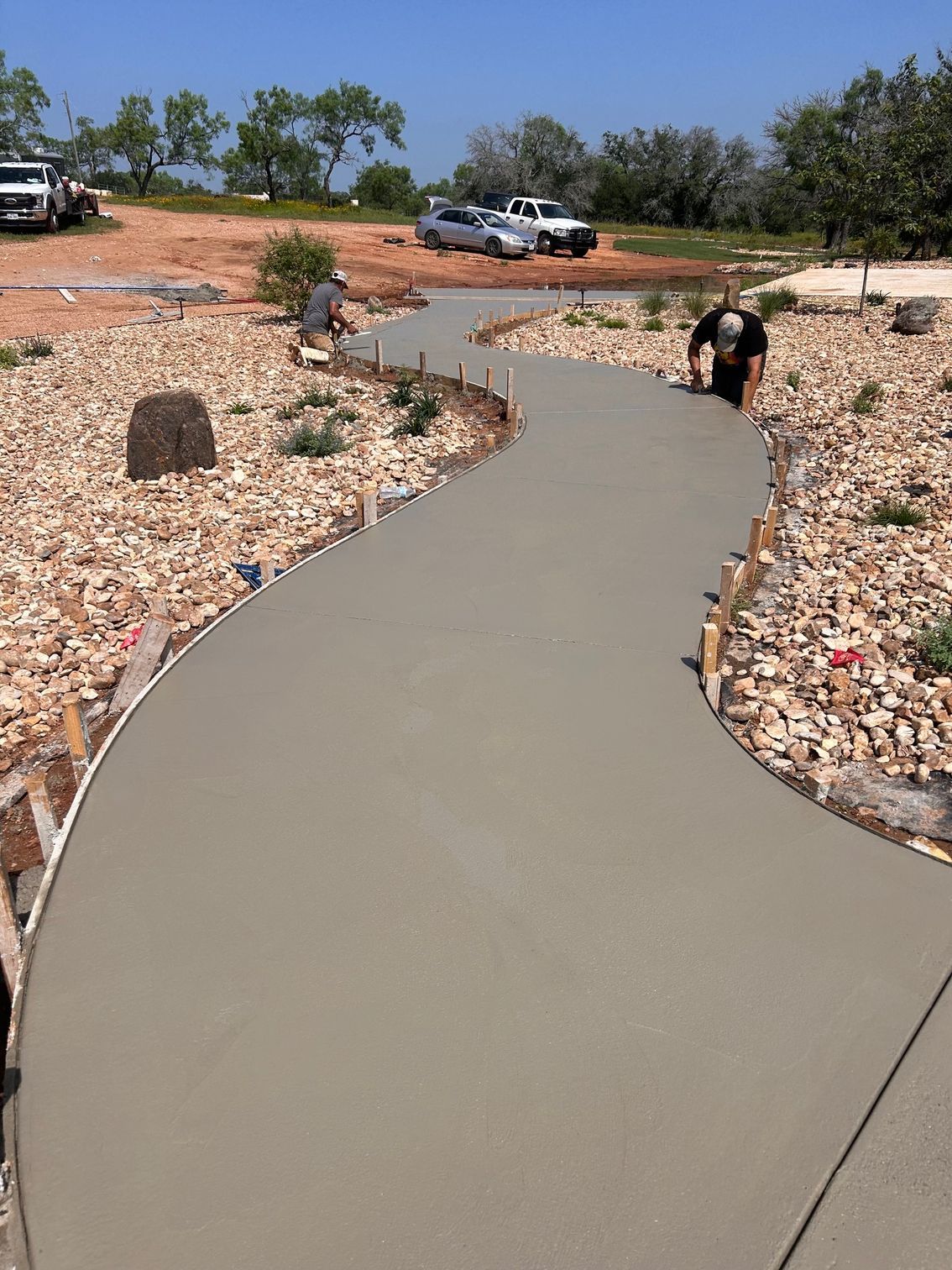 A man is working on a concrete driveway surrounded by rocks.