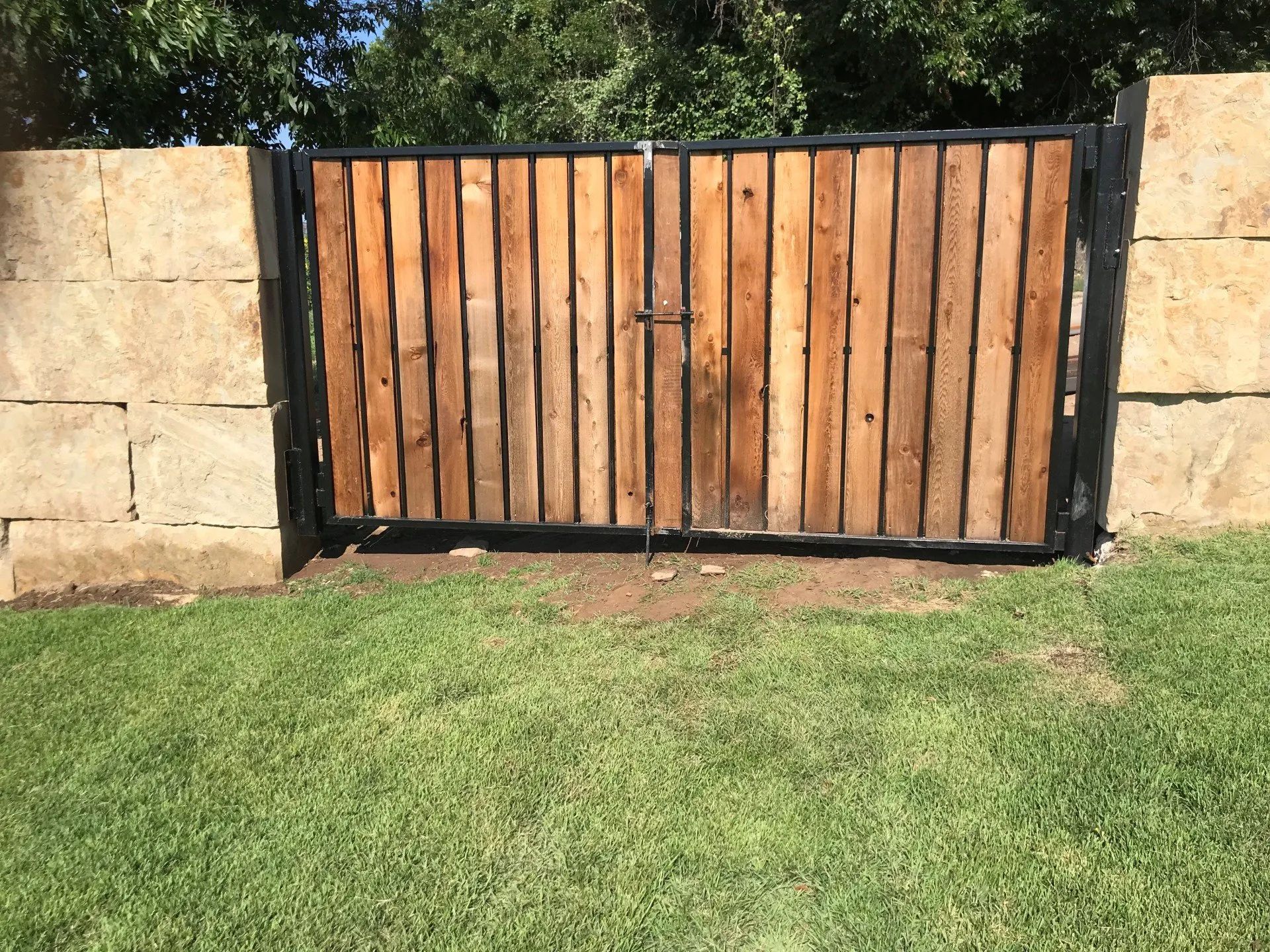 A wooden gate is sitting in the grass next to a stone wall