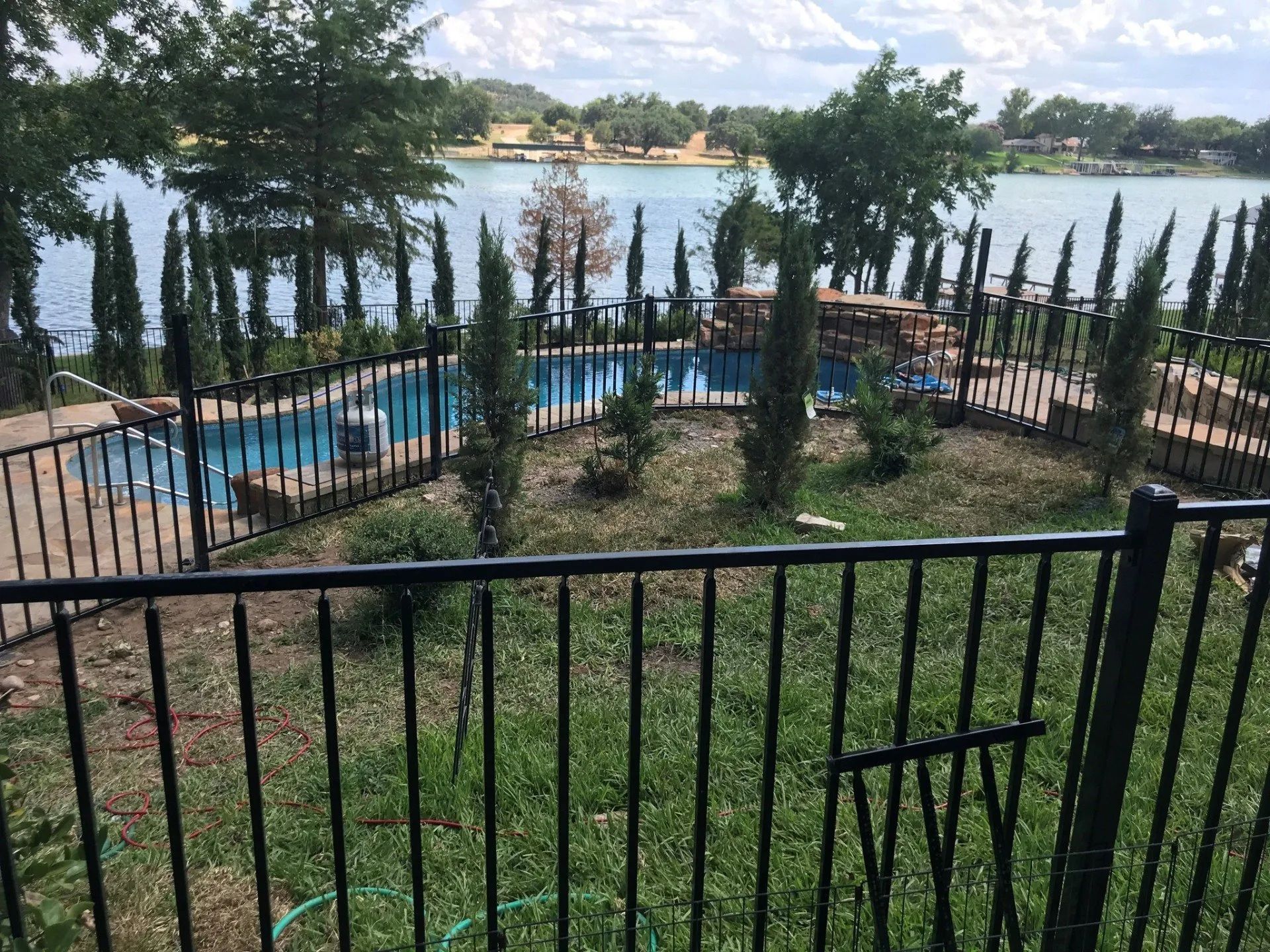 A black fence surrounds a swimming pool and a lake