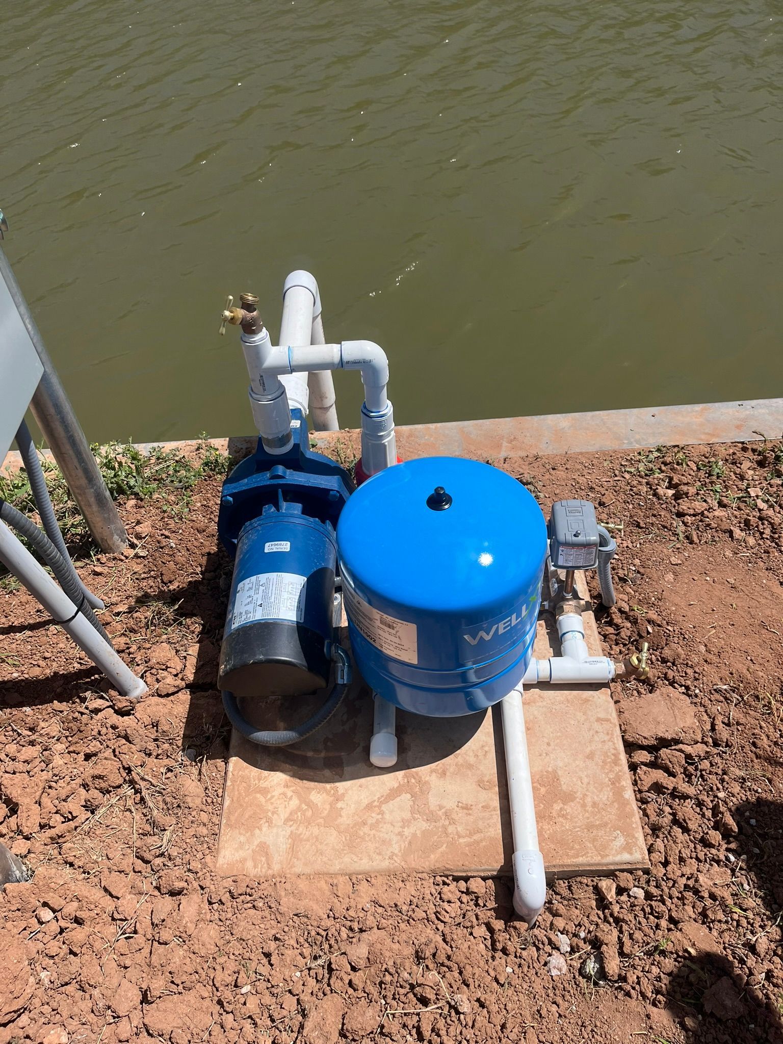 A blue water pump is sitting next to a body of water.