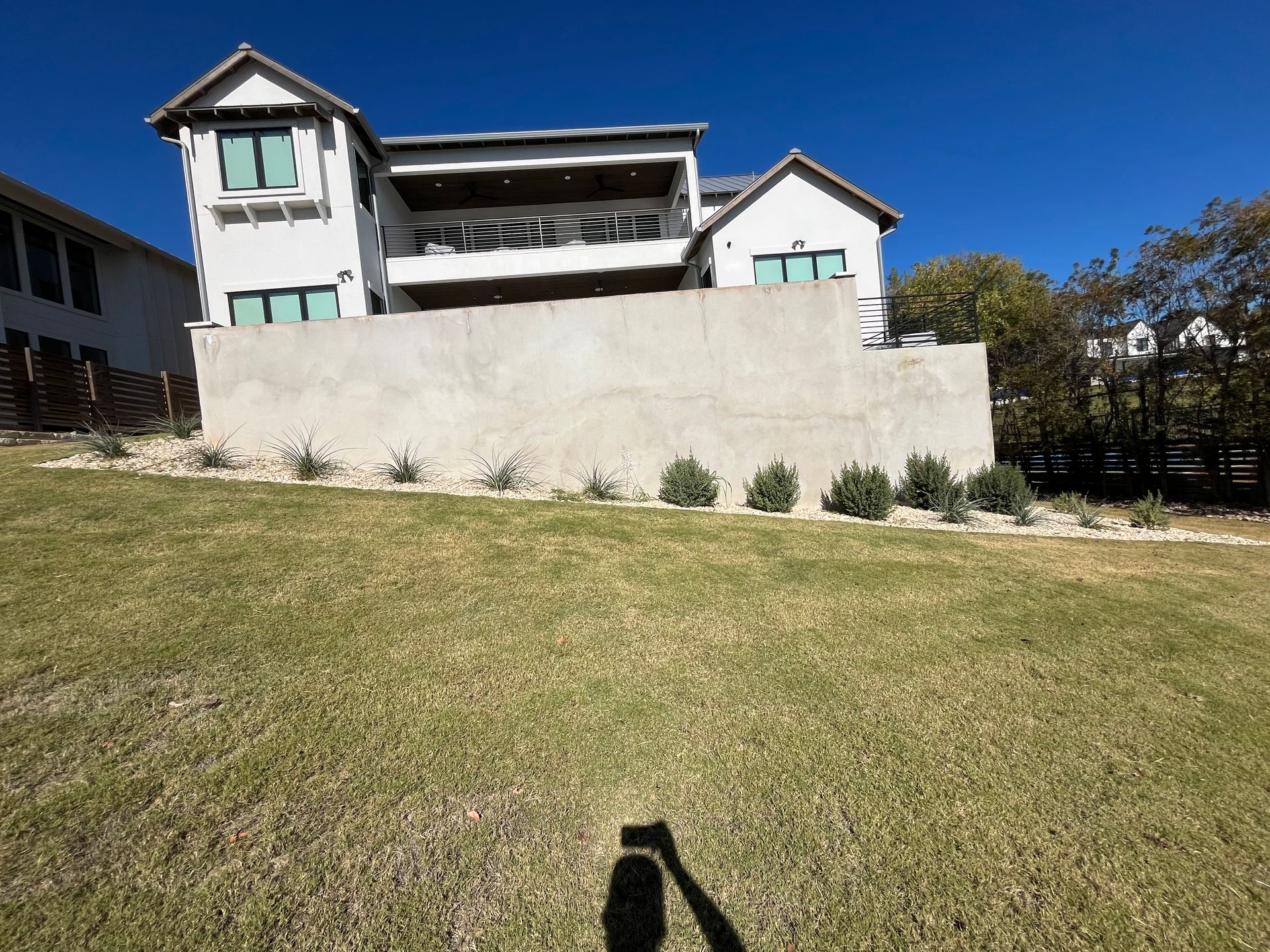 A shadow of a person is cast on the grass in front of a large house.