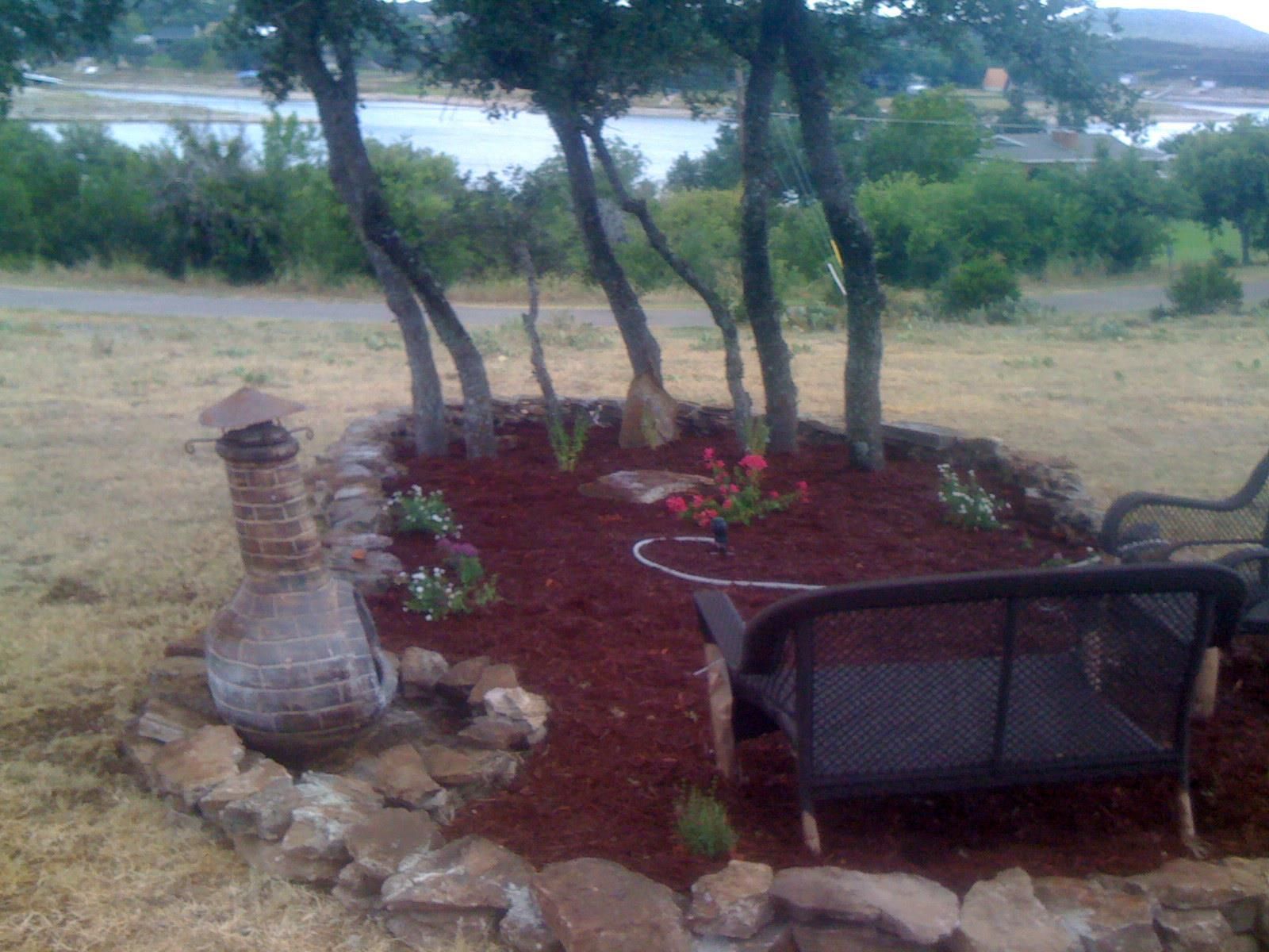 A bench sits in the middle of a garden with a fireplace in the background