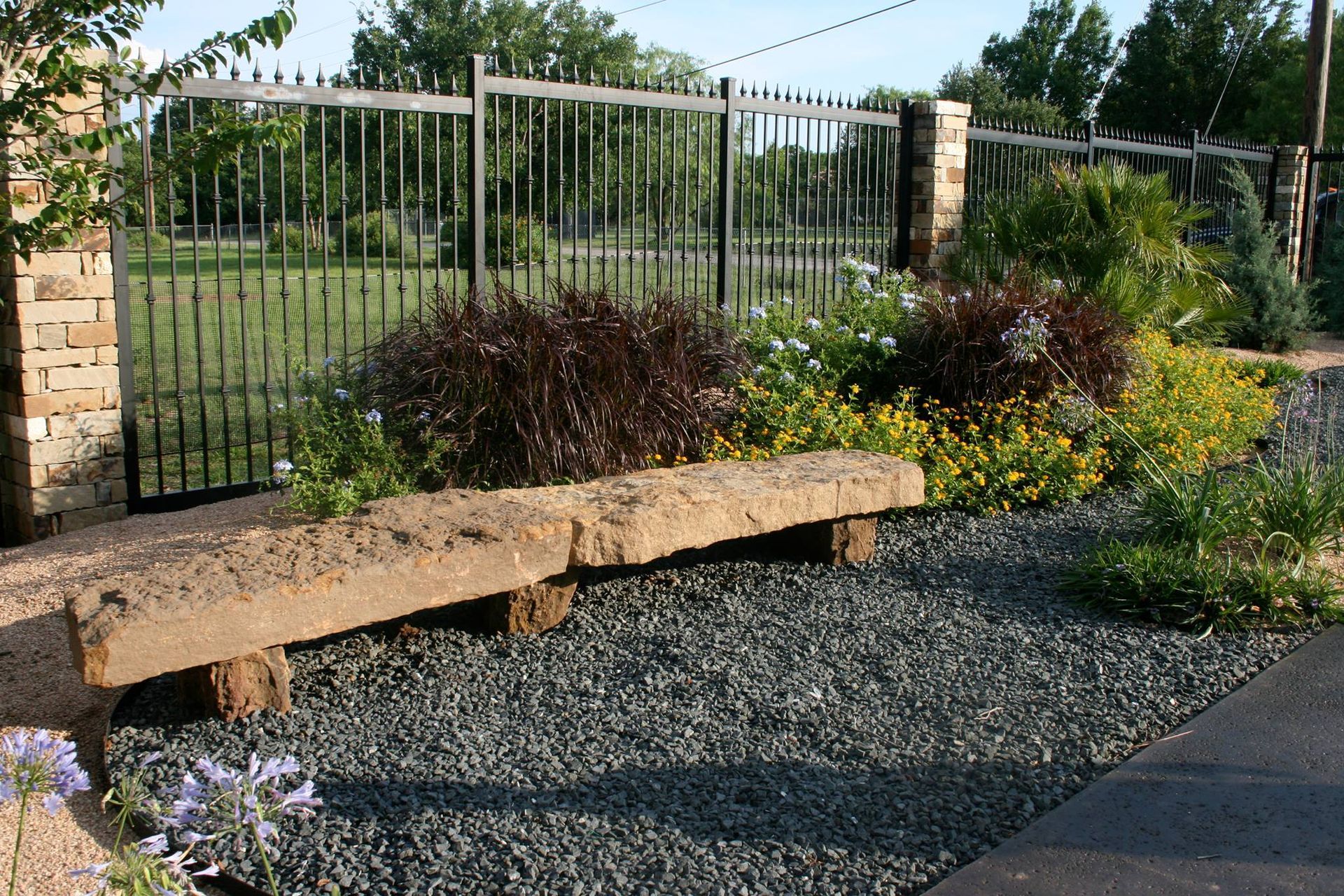 A stone bench sits in a garden surrounded by gravel and flowers